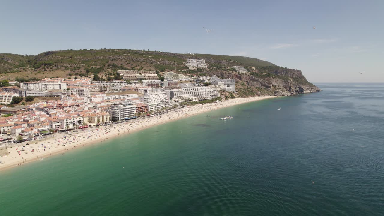 Ripresa aerea orbitale della bellissima costa di Sesimbra, mare verde e blu, gabbiani che volano da vicino.