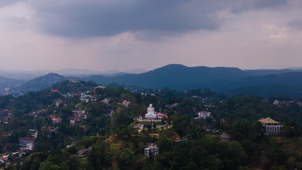 Beautiful tall white Bahirawakanda Vihara Buddha statue on one of the green hilltops in Kandy Sri Lanka as several vehicles drive on the winding road on a cloudy day. Hyperlapse drone shot