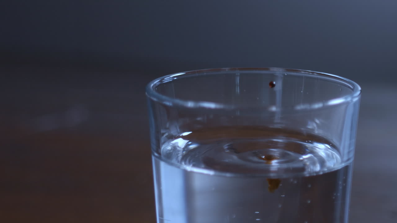Liquido scuro che gocciola in un bicchiere d'acqua e si diffonde