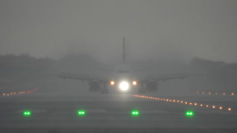 airplane approaches runway in thick fog, with bright lights illuminating the path during heavy rain