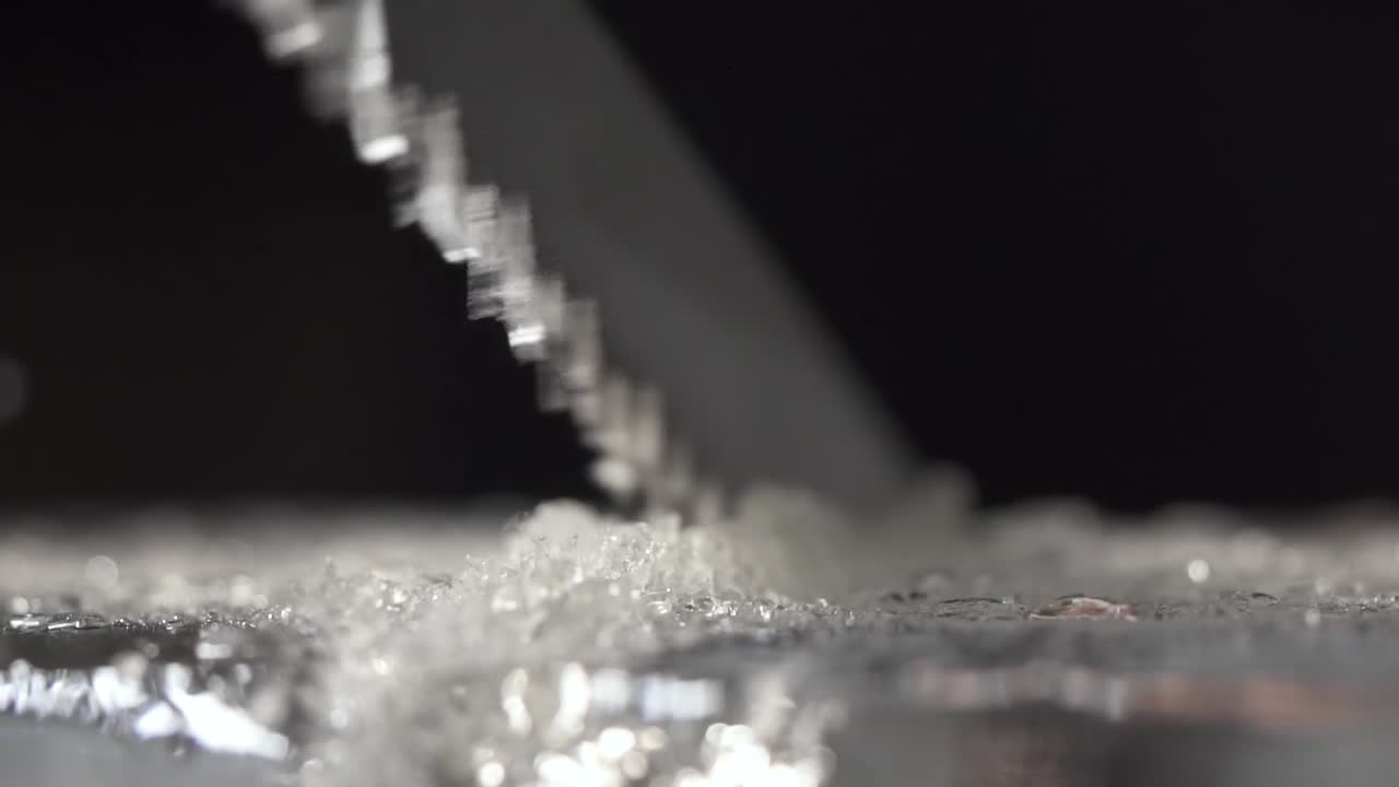 A bartender is cutting the ice block to smaller pieces for cocktail service by using a long toothed knife.