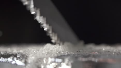 a bartender is cutting the ice block to smaller pieces for cocktail service by using a long toothed knife.