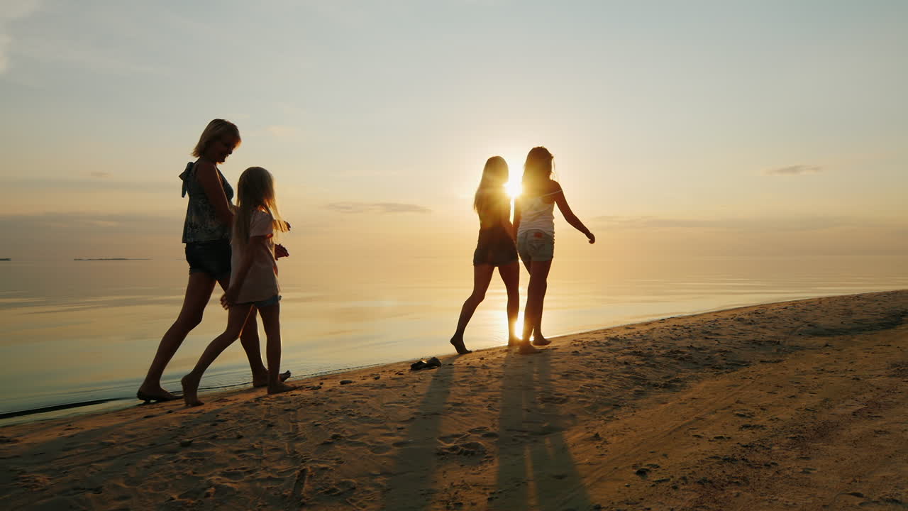 자녀를 둔 부모는 해변의 저녁 일몰에서 모래를 걷습니다.