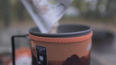 shallow depth static shot of oatmeal being poured into camp stove pot