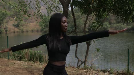 Medium-shot-of-a-girl-stretching-in-a-warrior-pose-by-the-lake