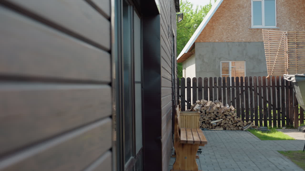 Serene backyard featuring wooden bench, stacked firewood, metal outdoor hot tub with chimney, wooden swing under canopy, partially constructed building, and lush green lawn bordered by dark fence