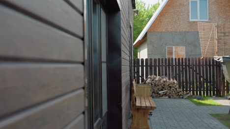 serene backyard featuring wooden bench, stacked firewood, metal outdoor hot tub with chimney, wooden swing under canopy, partially constructed building, and lush green lawn bordered by dark fence