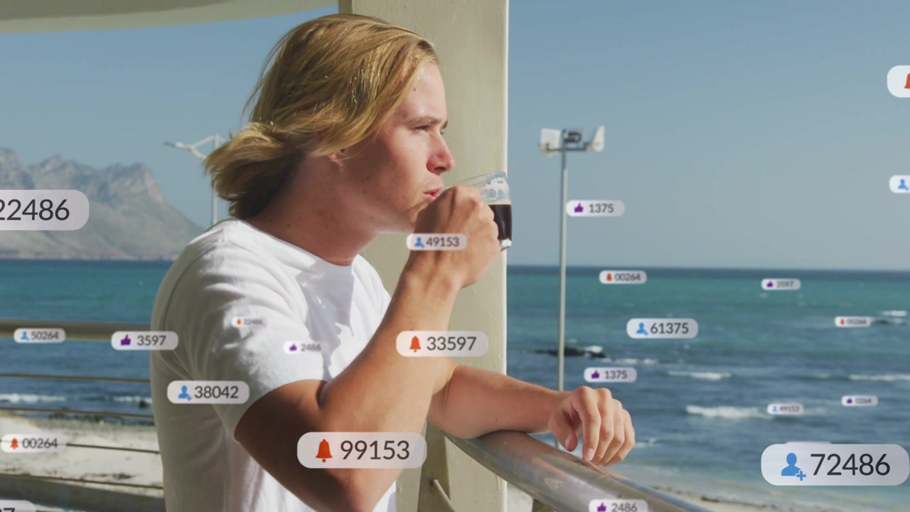 Man leaning on metal railing at seaside holding clear cup with notification overlays multiplying