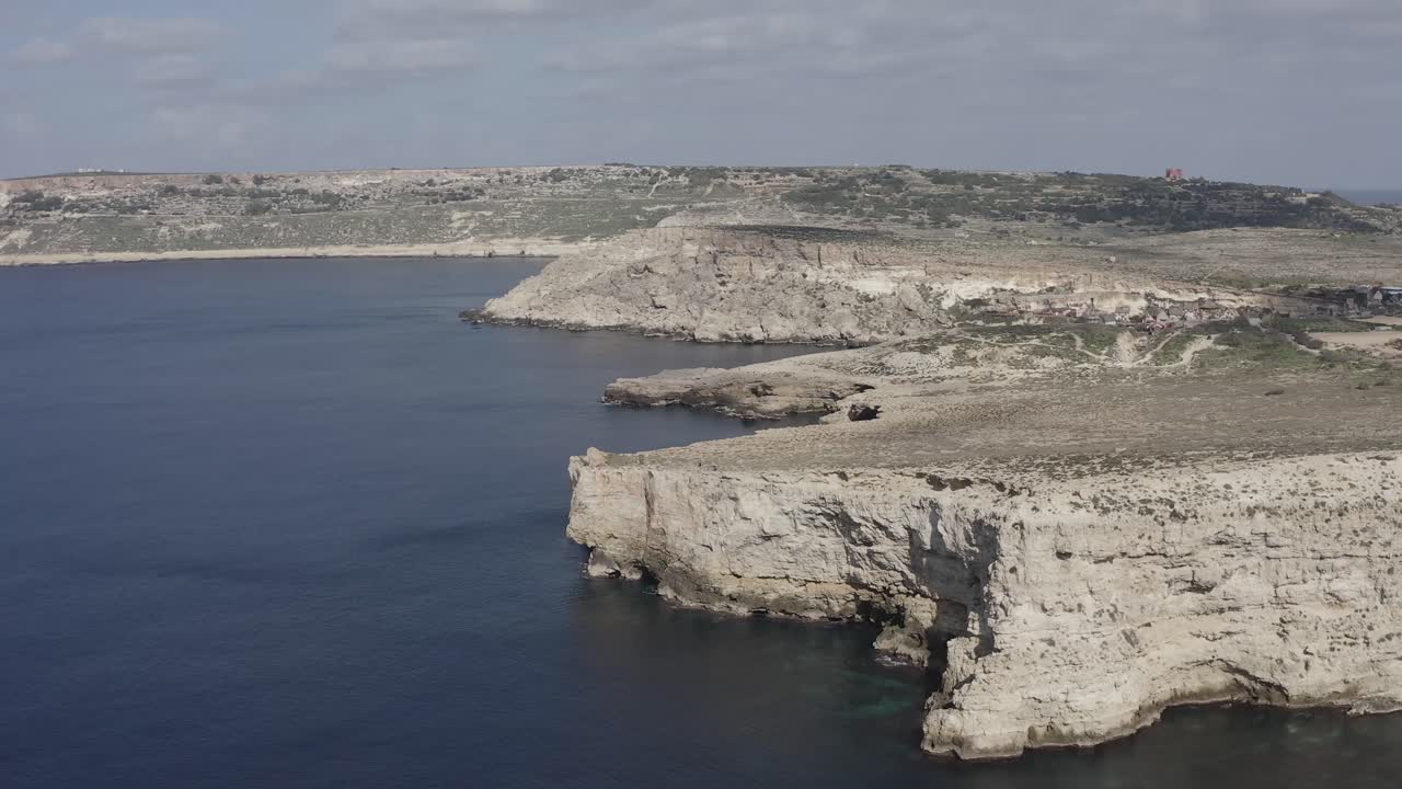 A drone flies backward along Malta’s dramatic dry cliffs, revealing rocky coasts, blue-grey sea, and expansive sky
