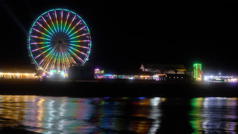 Paseo-En-Noria-Y-Diversiones,-Por-La-Noche-Con-Luces-Que-Se-Reflejan-En-La-Marea-Entrante-En-El-Muelle-Central,-Blackpool,-Lancashire,-Inglaterra,-Reino-Unido.