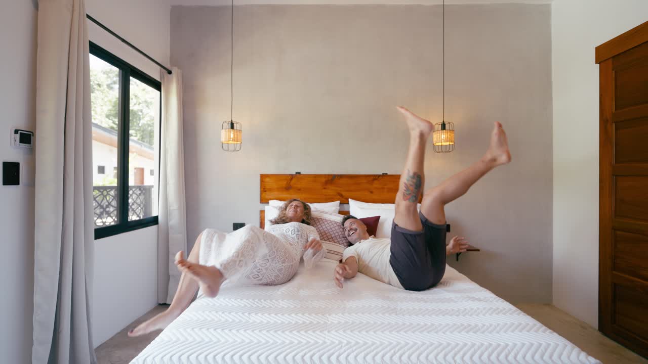 Casal Feliz Pula Divertidamente na Cama e Se Deita de Mãos Dadas