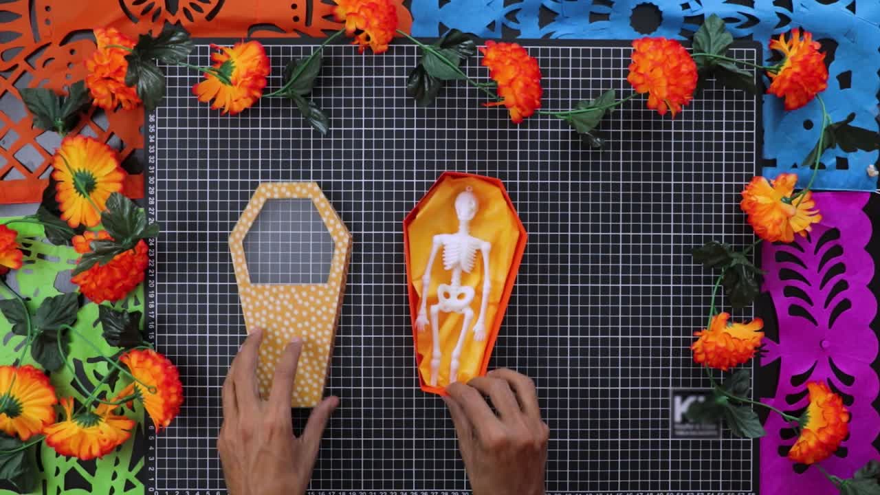 Crafting coffin cardboard box with skeleton and marigolds for Day of the Dead, top down view