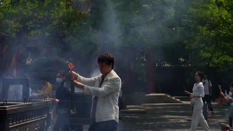man in beijing's lama temple burns incense in a large ceremonial burner as smoke rises