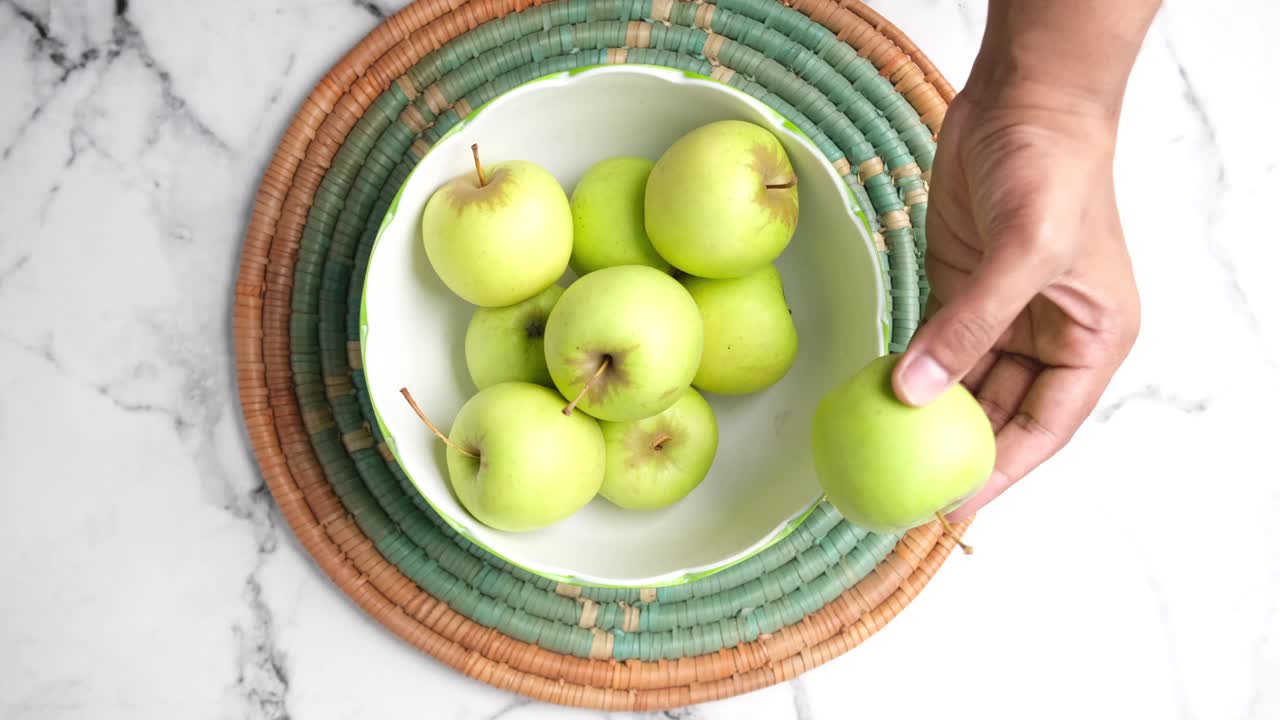 Mano che raccoglie una mela verde da una ciotola