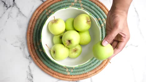 hand picking a green apple from a bowl