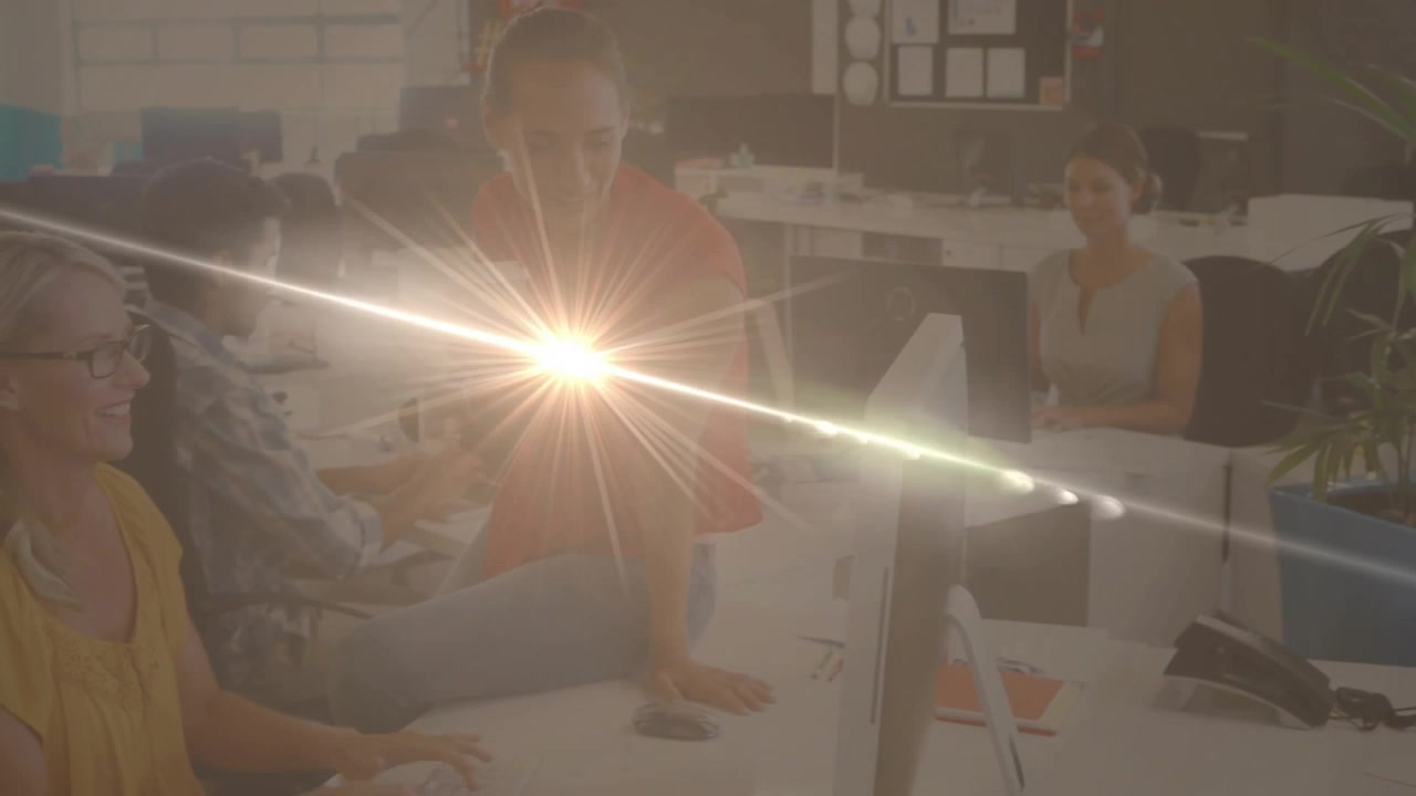 Diagonal lens flare initiating woman in red holding cup, engaging yellow coworker in office update