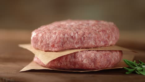 raw burger on paper with rosemary rotates.