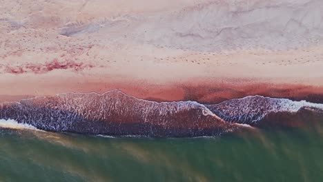 drone glides down over sunset shore as waves mix with vibrant sand colors