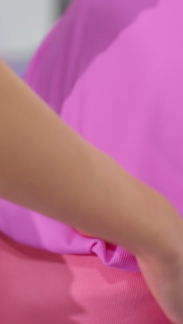 primer plano de manos ayudando a una mujer con ropa deportiva rosa mientras realiza un estiramiento de la columna vertebral, el fondo borroso sugiere un gimnasio o estudio de fitness, enfatizando la orientación y el apoyo profesionales