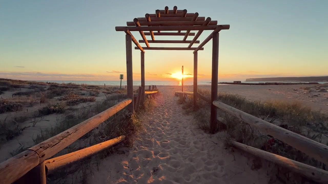 Går på en træpromenade, der fører til en smuk strand ved solnedgang, hvilket skaber en fredelig og indbydende atmosfære, Barbate, skud fra førstepersonsperspektiv.