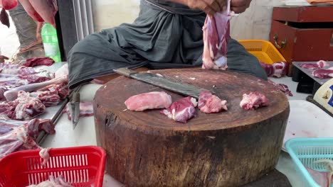 butcher cutting raw meat in india with big knife. he is making pieces for keema, kabab, nalli, paya muslim dishes.