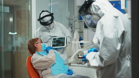 stomatologist in protective suit reviewing x-ray of tooth using tablet