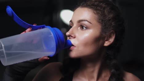 Sporty-girl-drinking-thirstily-from-a-water-bottle-after-some-exercising-in-a-gym.-Slow-Motion-shot