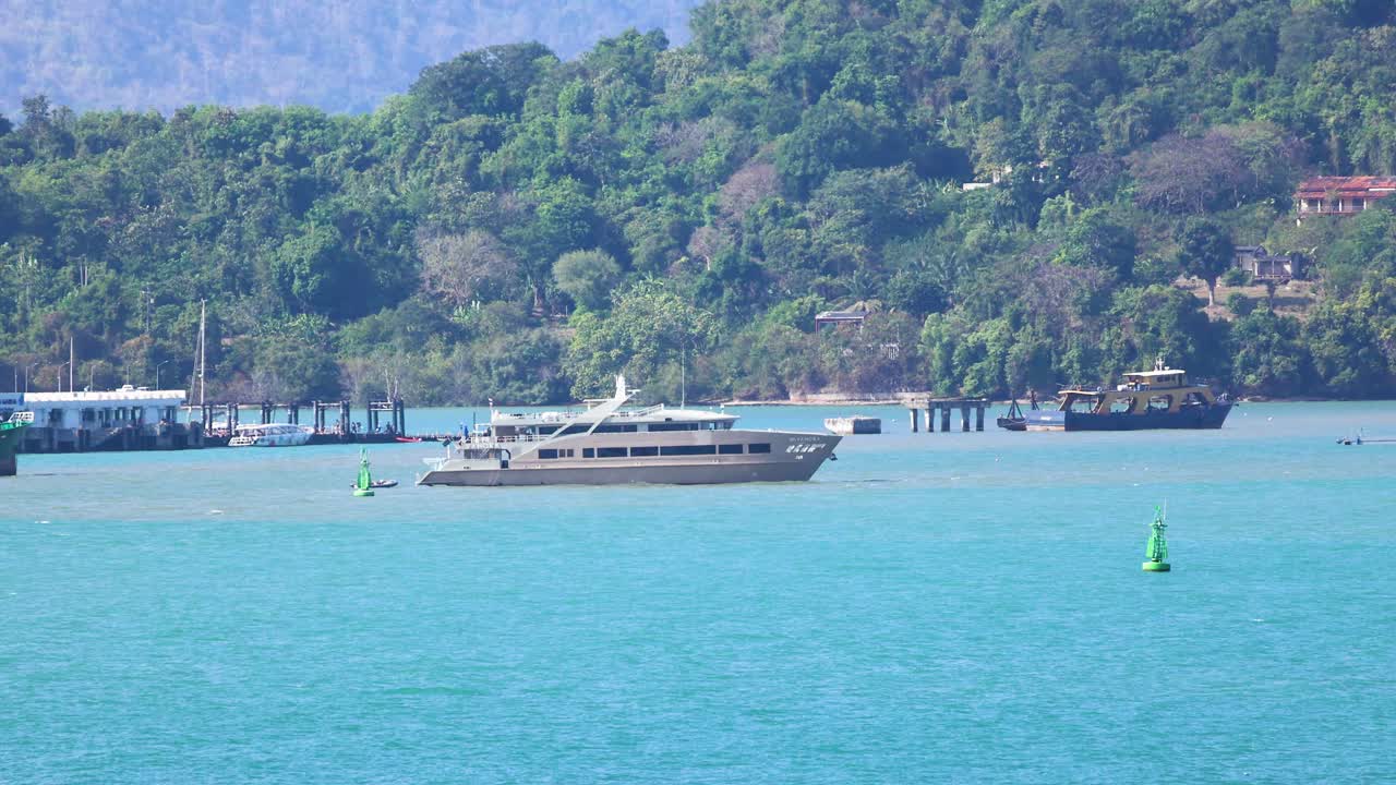 A luxury yacht glides across Phuket's turquoise sea, set against lush green hills under bright daylight