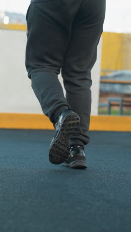 vista trasera de un atleta corriendo en una arena deportiva con enfoque en las piernas y los zapatos, mostrando movimiento dinámico, aptitud y acción contra el límite amarillo y el fondo urbano
