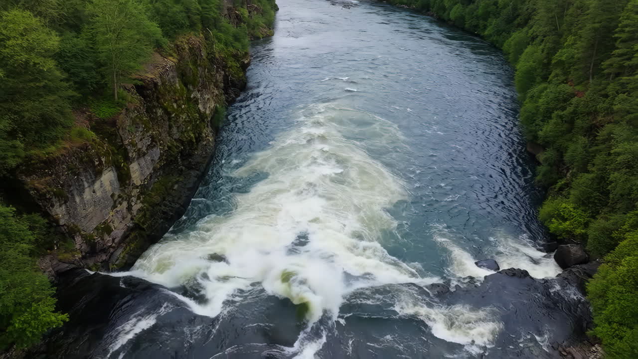 Panoramic view of a powerful waterfall flowing into a river surrounded by lush green forests and rocky cliffs