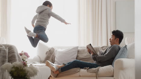 funny-little-asian-boy-jumping-onto-sofa-playing-with-father-happy-dad-enjoying-playful-game-with-son-at-home-4k