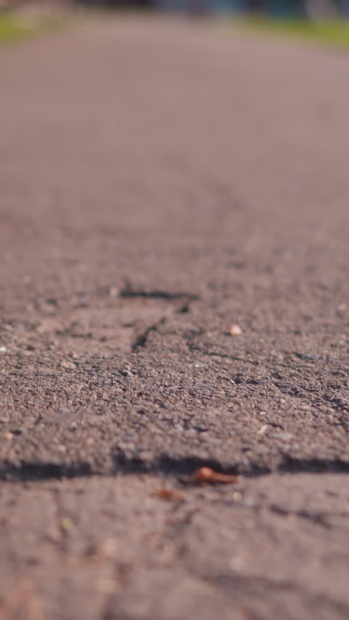 눈에 띄는 균열과 거친 패치가있는 균열, 텍스처 도로 표면의 클로즈업, 녹색 잎자루와 함께 흐릿한 배경으로 이어집니다.