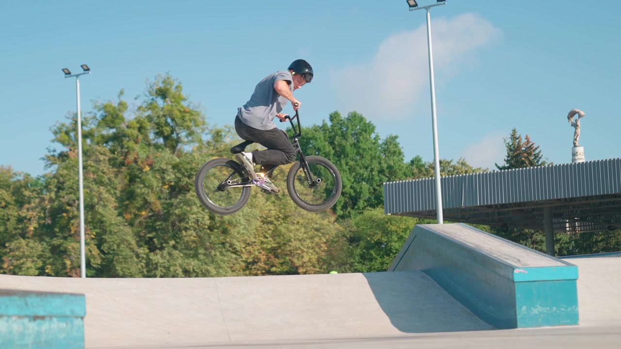 Giovane uomo in bici BMX esegue un salto in uno skatepark al rallentatore