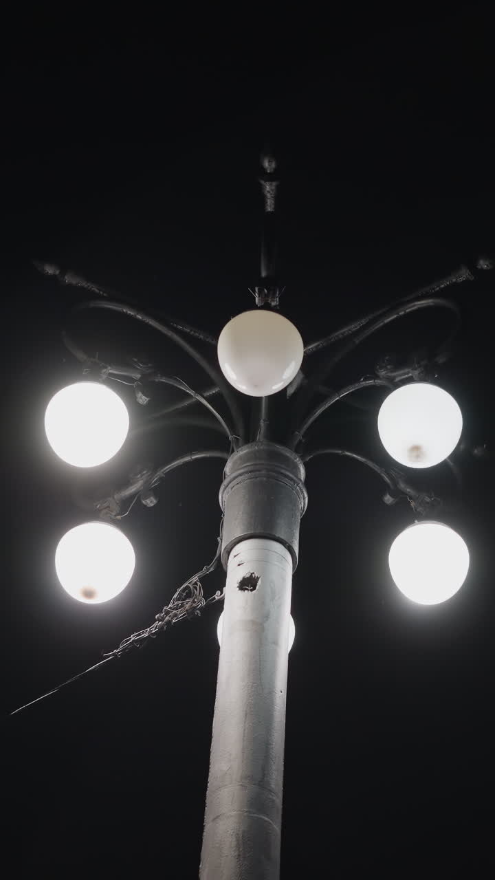 vista de cerca de un poste de farola con cinco bombillas iluminadas contra un cielo oscuro. una de las bombillas está parpadeando