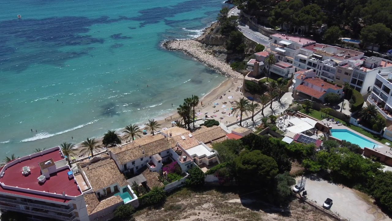 Video statico aereo con drone della spiaggia di El Portet a Moraira, Spagna, ripreso dall'entroterra. Acque cristalline mediterranee, costa e villaggio panoramico