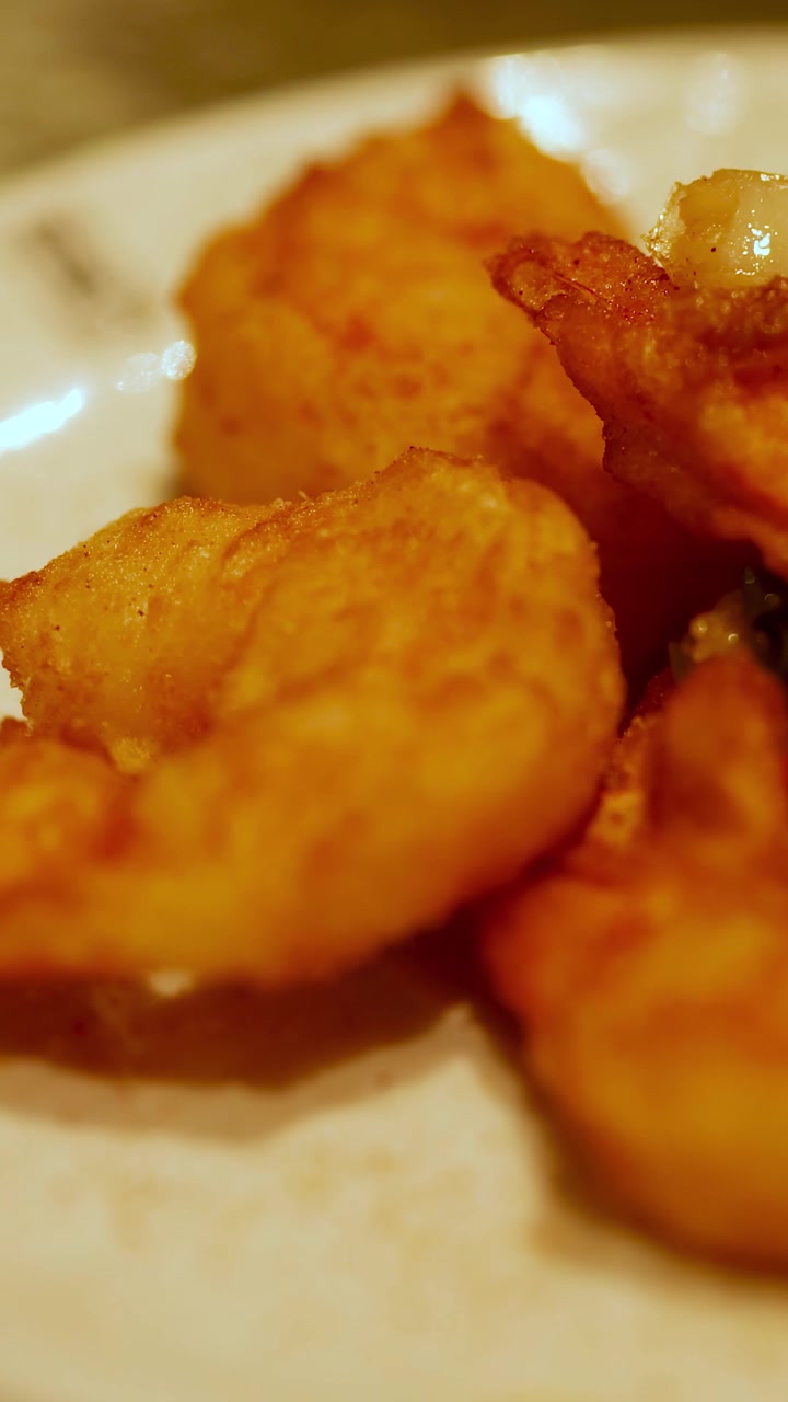 Primo piano di gamberi fritti croccanti su un piatto bianco, che mette in risalto ricche tonalità dorate e consistenze appetitose sotto un'illuminazione calda.