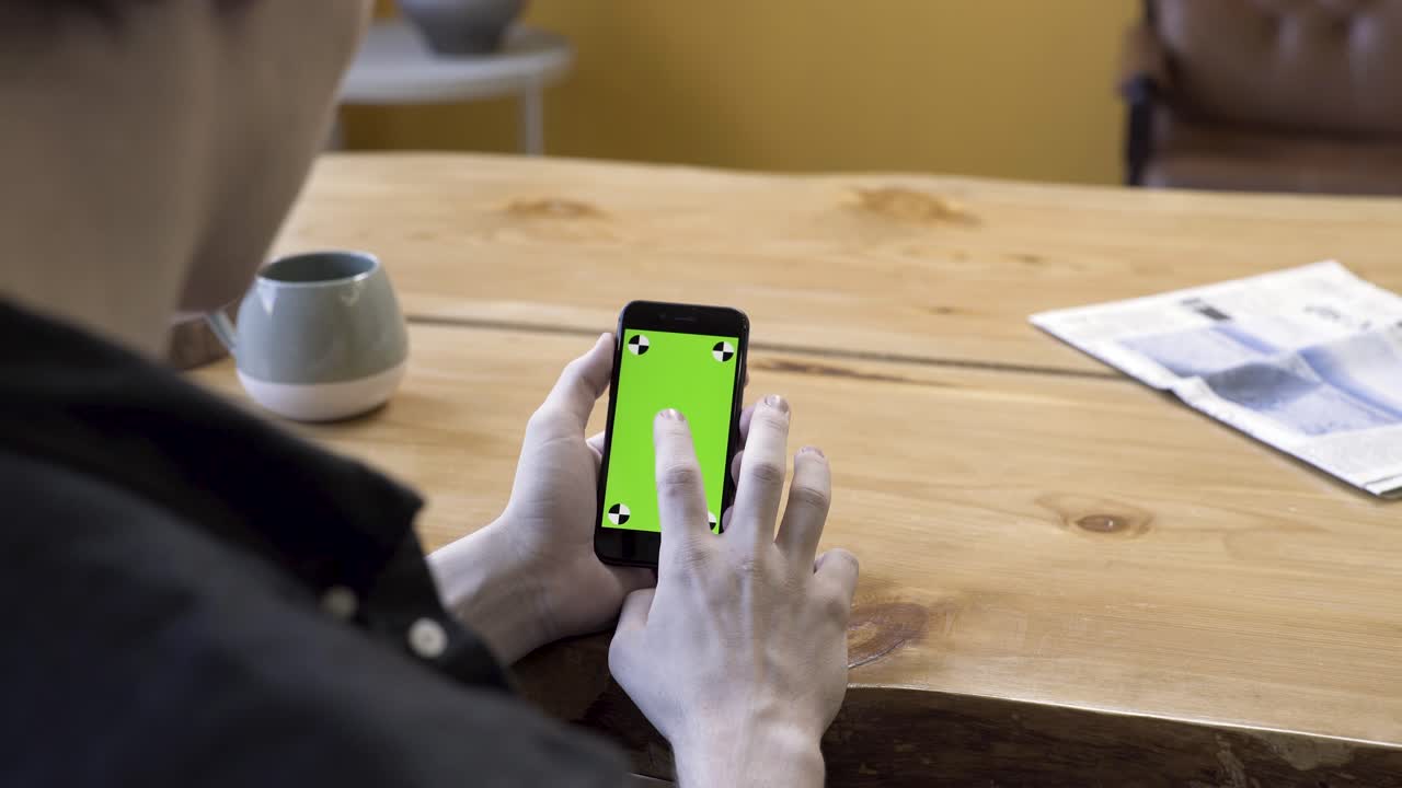 나무 테이블 위에 초록색 화면을 가진 스마트폰을 사용하는 사람