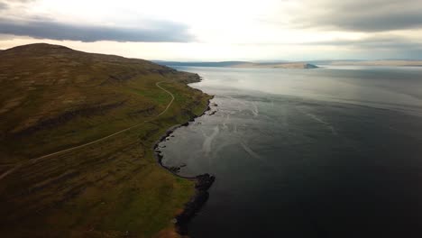 Aerial-panoramic-landscape-view-of-Iceland-nordic-coast,-with-ocean-waves-crashing-on-the-shoreline,-at-dusk