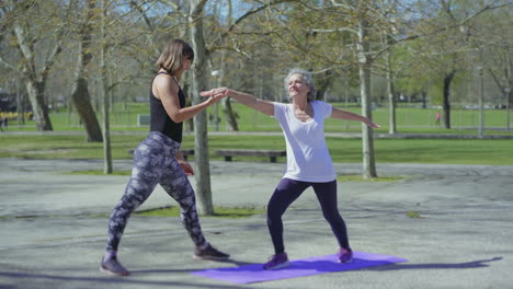 una mujer mayor sonriente practicando yoga con un entrenador en el parque.