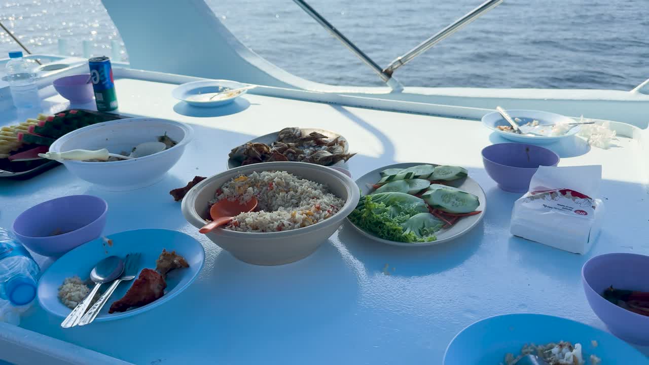 A serene meal setup on a boat with ocean views, featuring fresh seafood and vibrant tropical fruits under bright daylight