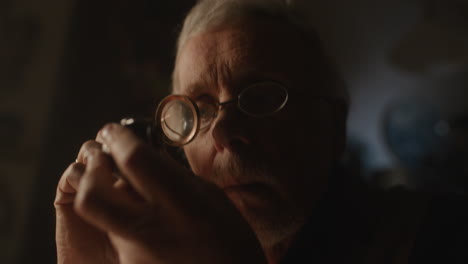 older passionate man evaluates an old silver skull watch in his office at night