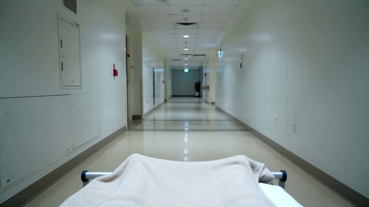 Barella coperta in movimento che scorre lungo il corridoio dell'ospedale dopo il trasferimento, mostrando le sponde della coperta beige