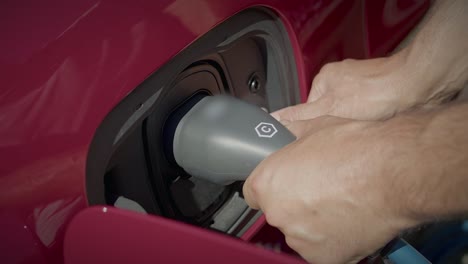 close up of hands inserting grey charger plug of electric hybrid car into connector