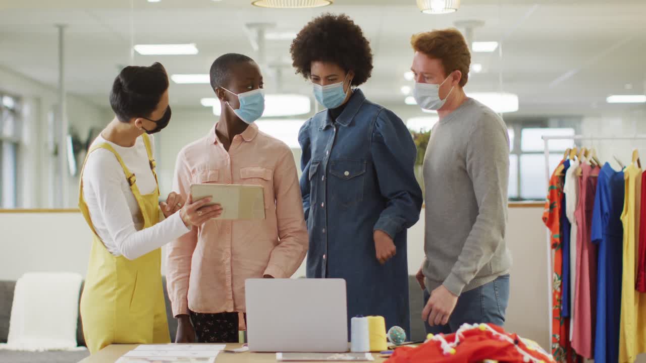 Diverse group of male and female business colleagues wearing face masks and working in office