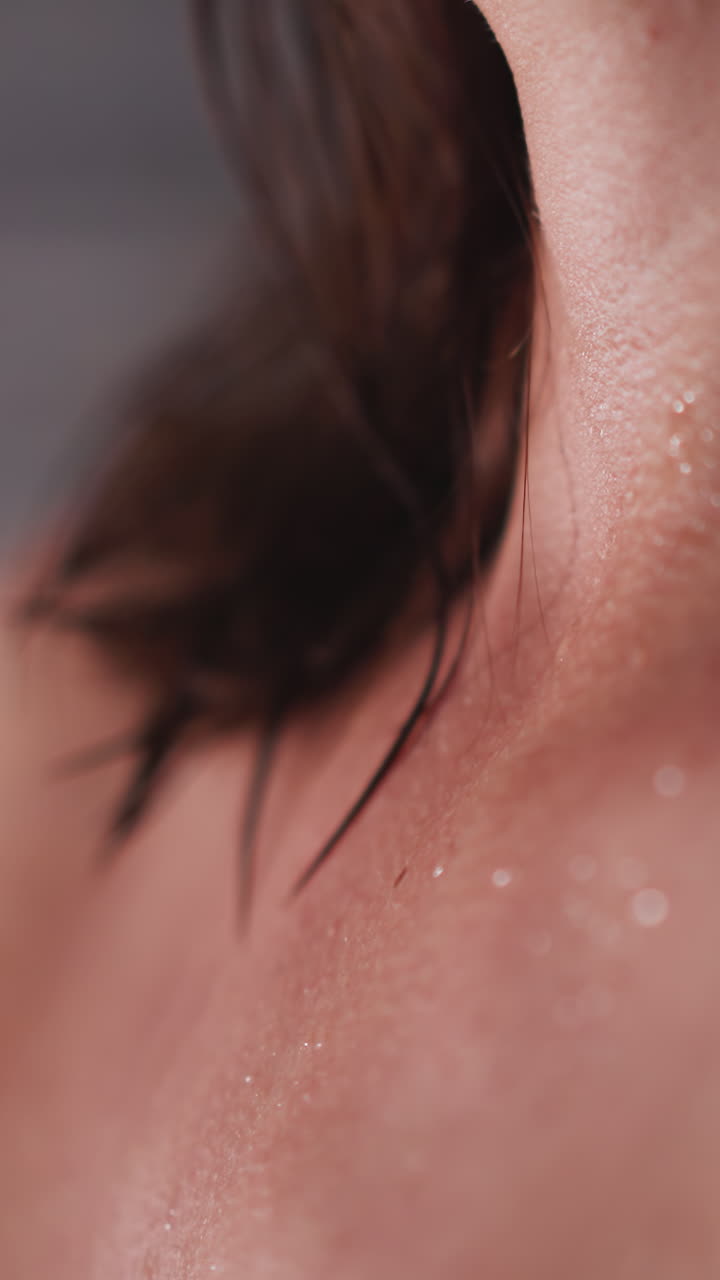 목에 여드름이 있는 여자가 화장실에서 샤워를 하고, 피부 문제가 있는 여인이 화장실에 서 있다.