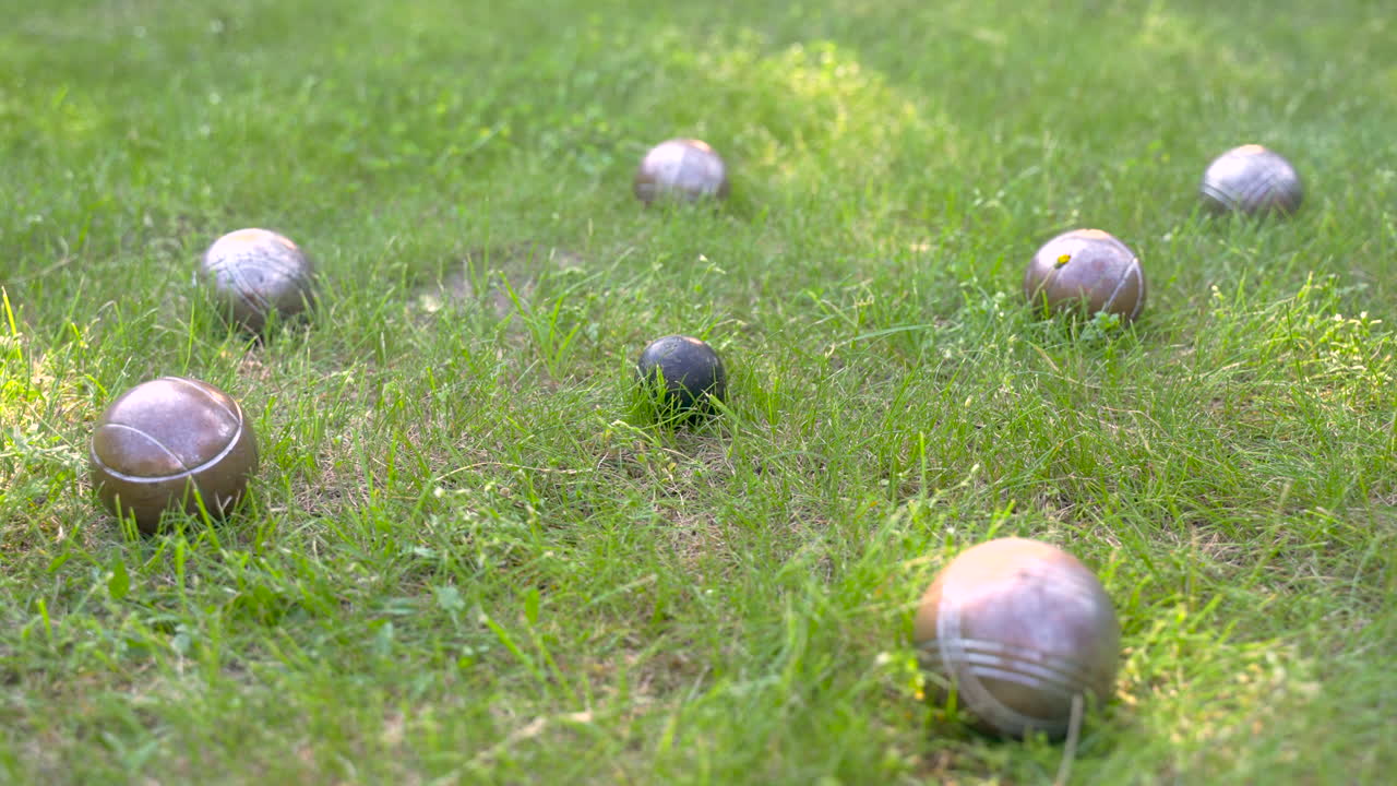 공원의 잔디에 있는 다른 공으로 둘러싸인 검은 금속 금속 페탕크 공을 확대하는 카메라