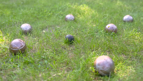 caméra zoomant sur une boule de pétanque en métal noir entourée d'autres boules sur l'herbe du parc