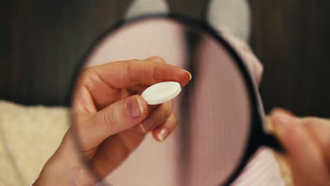 woman examining a pill under a magnifying glass