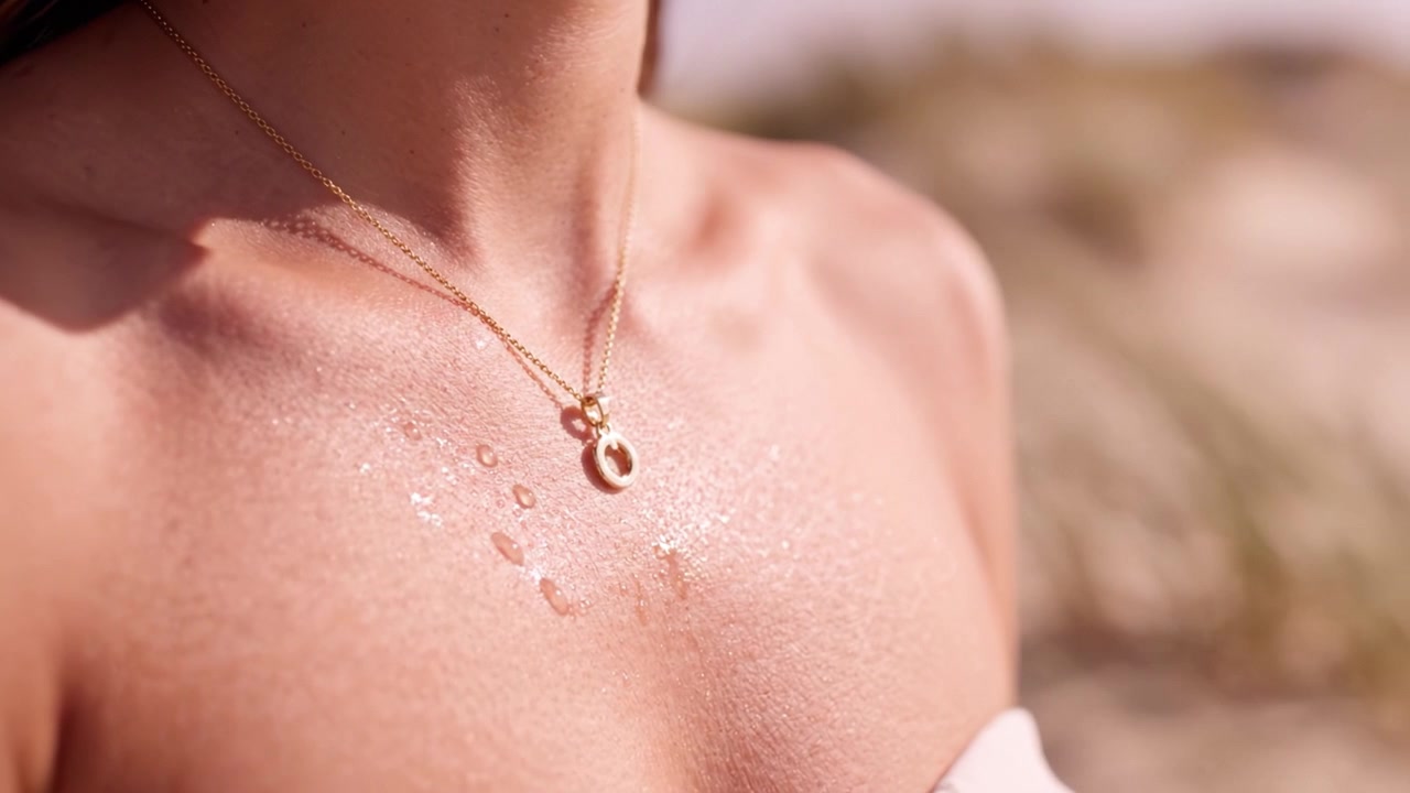 Una rappresentazione ravvicinata di un corpo splendente adornato con una delicata collana d'oro, che evidenzia la connessione intima tra pelle e gioielli sotto la luce naturale.