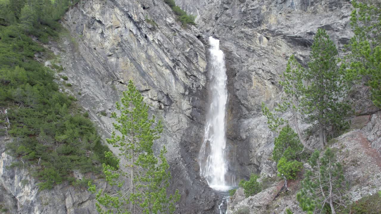 imágenes aéreas de drones que vuelan lentamente sobre el dosel de un árbol para revelar una espectacular cascada que cae en cascada sobre el borde de un acantilado de montaña en una piscina de inmersión en suiza